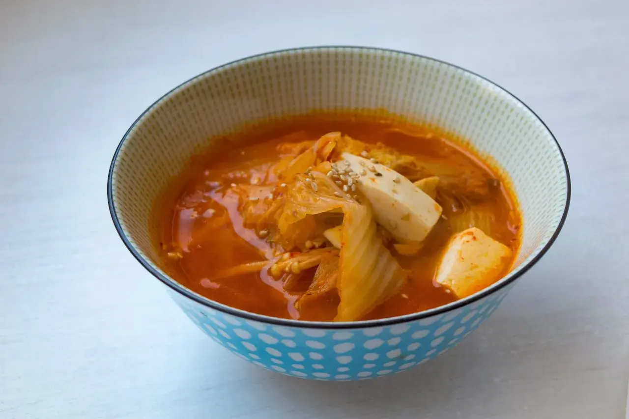 Eine Schüssel mit dampfender Kimchi-Suppe, garniert mit Tofuwürfeln und Sesam.