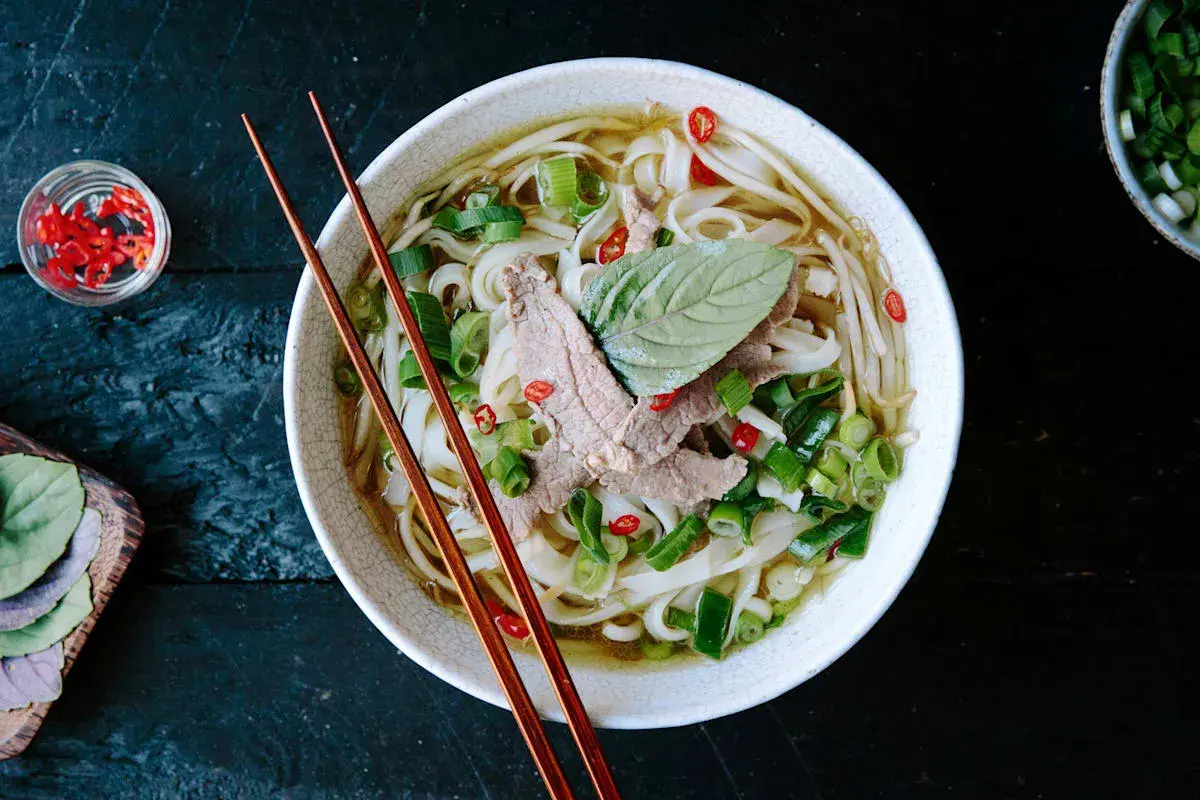 Eine Schüssel dampfendes Pho mit dünnen Rindfleischscheiben, Reisnudeln, Frühlingszwiebeln und Chili. Ein perfektes Pho-Rezept für kalte Tage.
