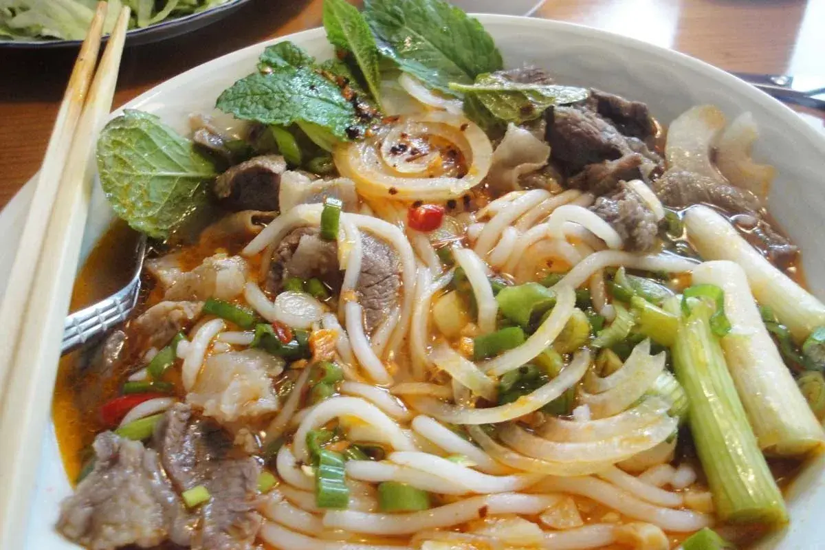 Eine Schüssel Bun Bo Hue mit Rindfleisch, Nudeln, Zwiebeln, Frühlingszwiebeln und Minze.