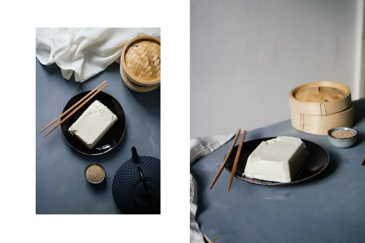 Ein Block Seidentofu auf einem Teller, daneben Stäbchen, eine Teekanne und Sesam. Was ist Seidentofu? Zart und cremig, ideal für asiatische Gerichte.