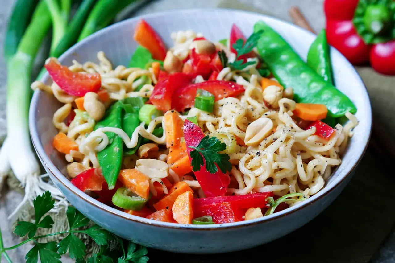 Bunter mie nudelsalat mit Erdnüssen, Paprika, Zuckerschoten und Karotten, garniert mit Petersilie.