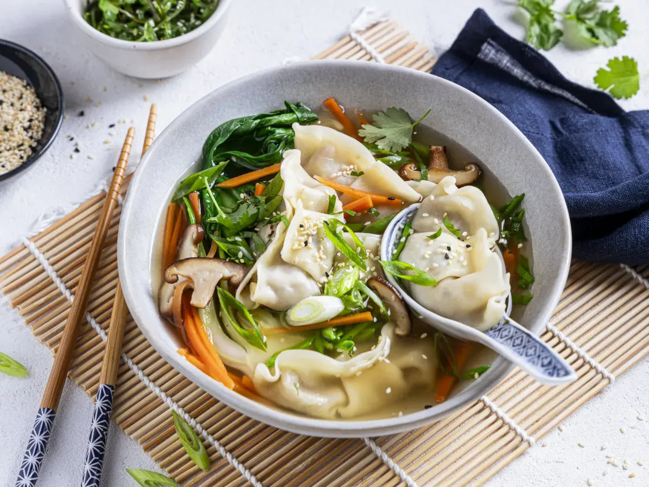 Eine dampfende Schüssel **Wantan Suppe** mit zarten Teigtaschen, Shiitake-Pilzen, Karotten und Frühlingszwiebeln, garniert mit Sesam.