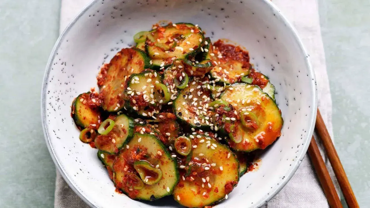 Ein Schüssel mit einem würzigen Gurken-Kimchi-Salat, garniert mit Sesam und Frühlingszwiebeln.