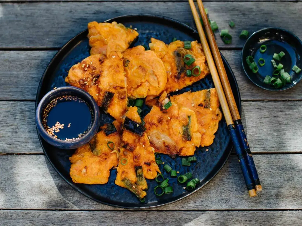 Knusprige Kimchi-Pfannkuchen mit Frühlingszwiebeln und Sesam, serviert mit Dip und Stäbchen.