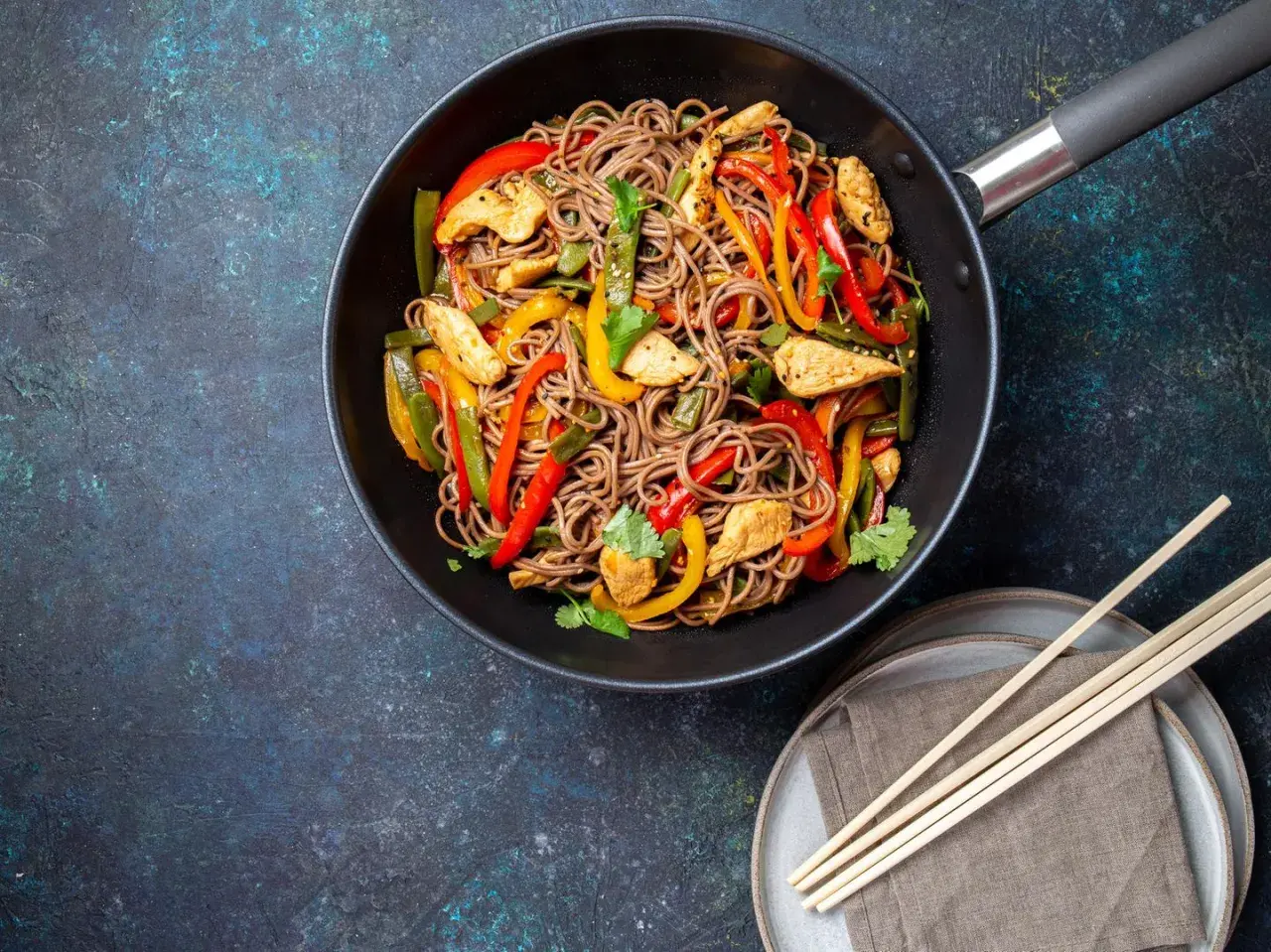 Wok-Gericht mit chinesischen Eiernudeln, Hähnchenstreifen und bunten Paprikastreifen, garniert mit Koriander.