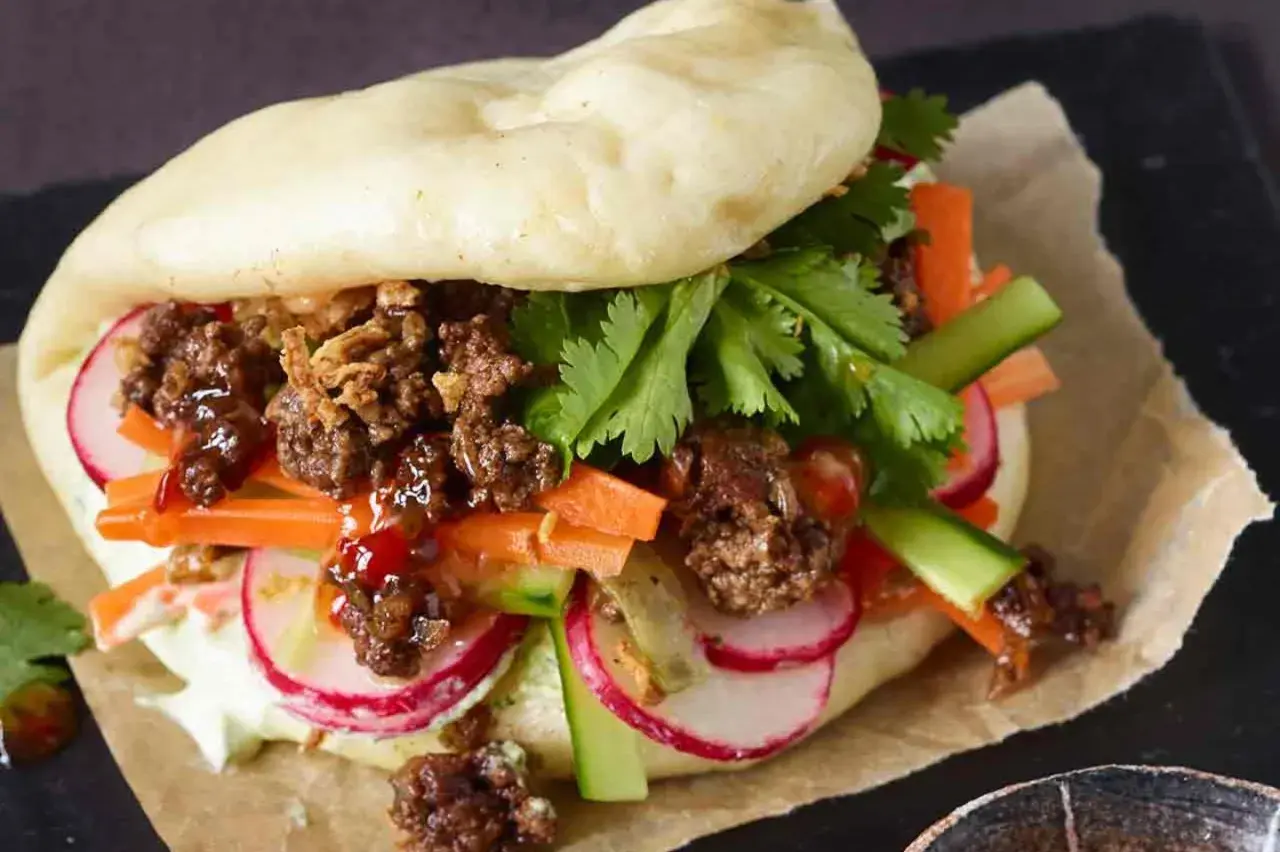 Ein saftiger Bao Burger mit Hackfleisch, knackigem Gemüse wie Karotten, Radieschen und Gurken, garniert mit Koriander.
