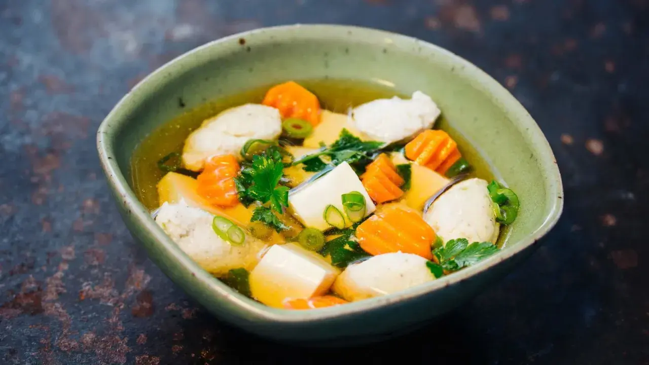 Eine Schüssel Hu Tieu Suppe mit Tofu, Karotten und Fleischbällchen, garniert mit Frühlingszwiebeln und Petersilie.