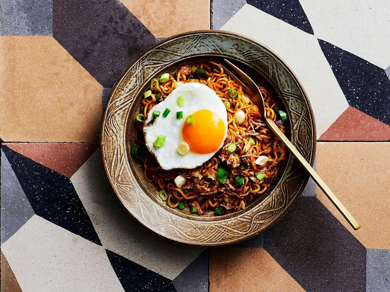 Schüssel mit Mie Goreng, garniert mit einem Spiegelei und Frühlingszwiebeln, auf einem geometrischen Fliesenmuster.
