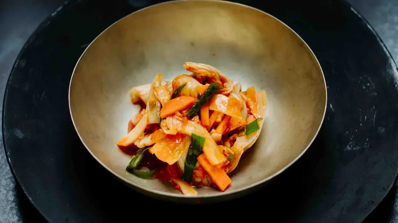 Kimchi mit Karotten und Frühlingszwiebeln, gewürzt mit Gochugaru, in einer Schale.