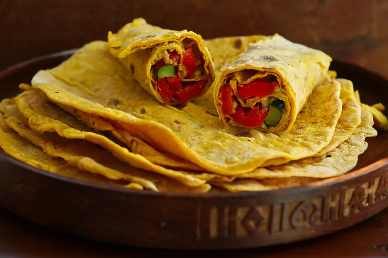 Chapati-Rezept: Fladenbrot gefüllt mit roten Paprika und Gurke, auf einem Stapel weiterer Chapati in einer Holzschale.