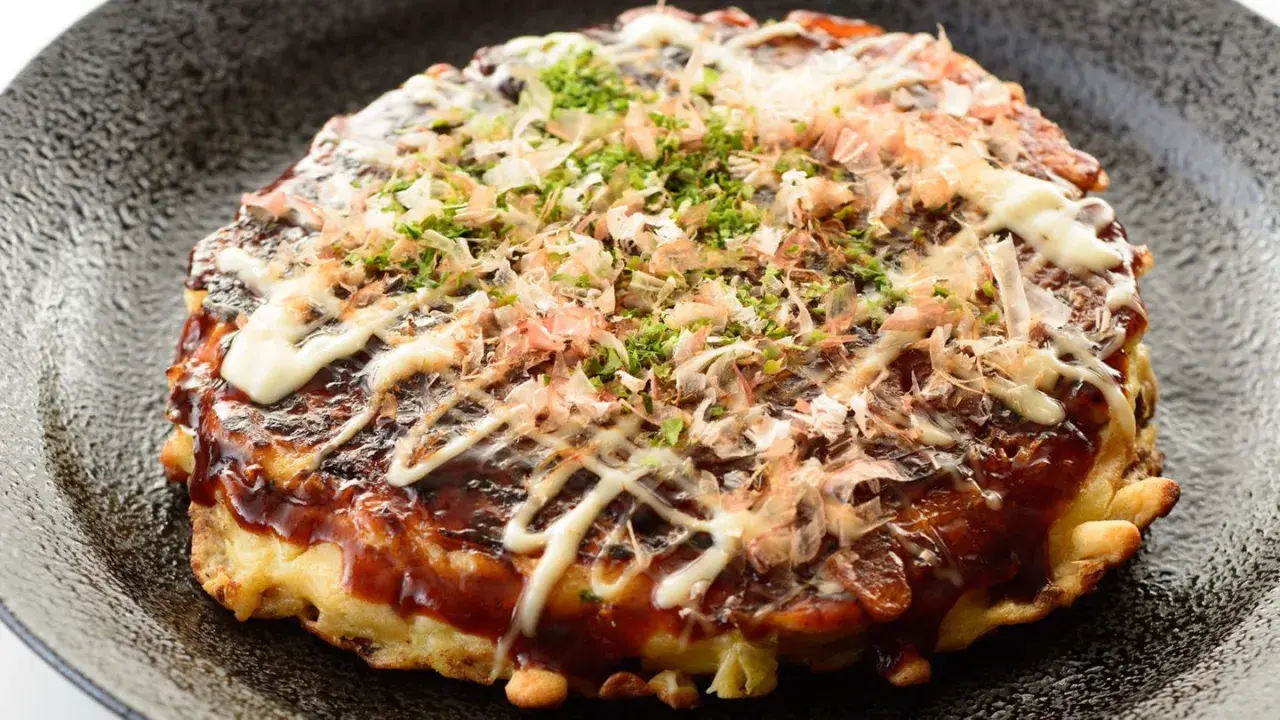 Ein herzhaftes Okonomiyaki Hiroshima, übergossen mit Sauce und Mayonnaise, bestreut mit Bonitoflocken und Schnittlauch.
