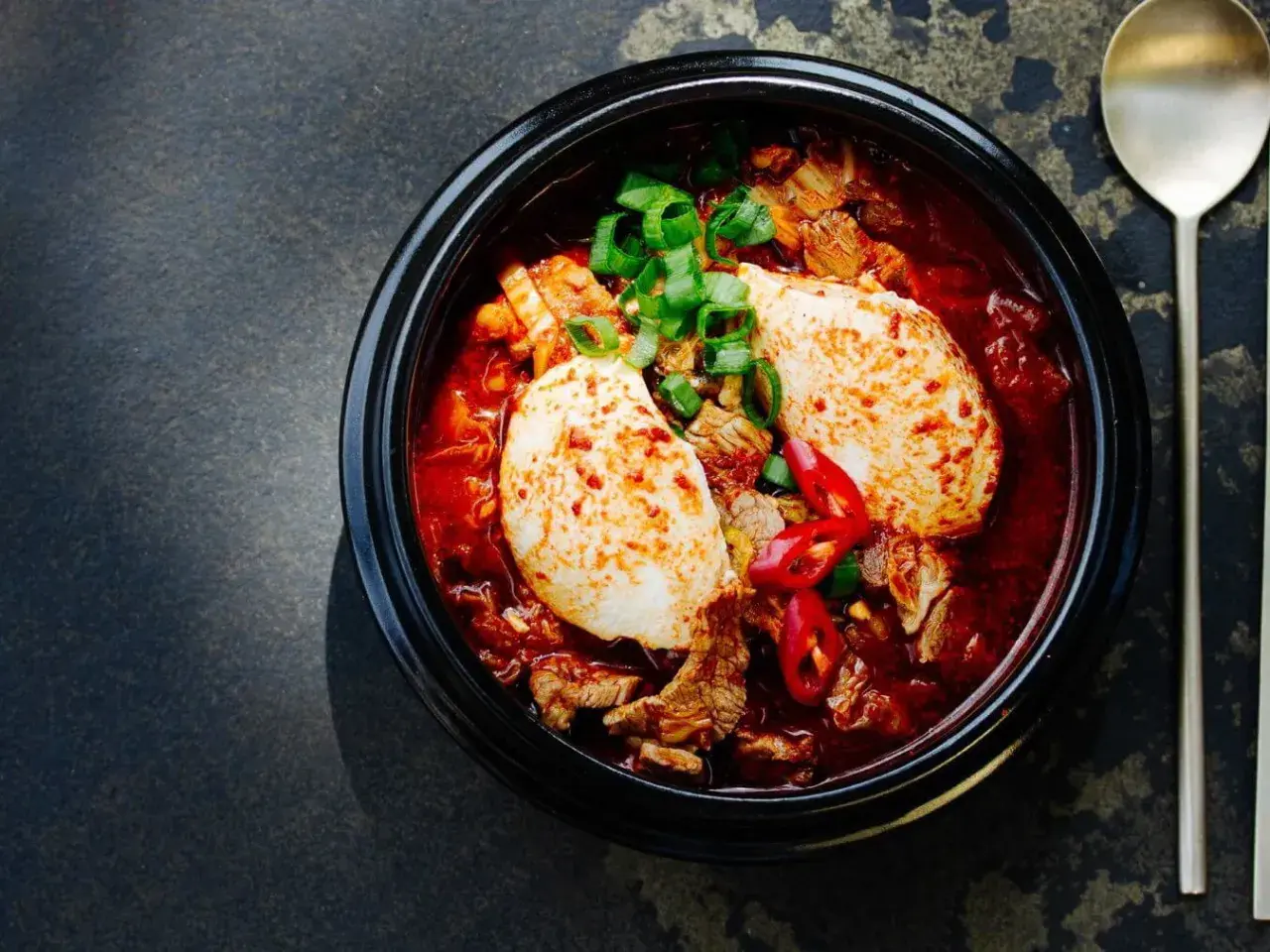 Herzhaftes Kimchi Jjigae mit Tofu, Rindfleisch und Frühlingszwiebeln, garniert mit Chilischeiben.