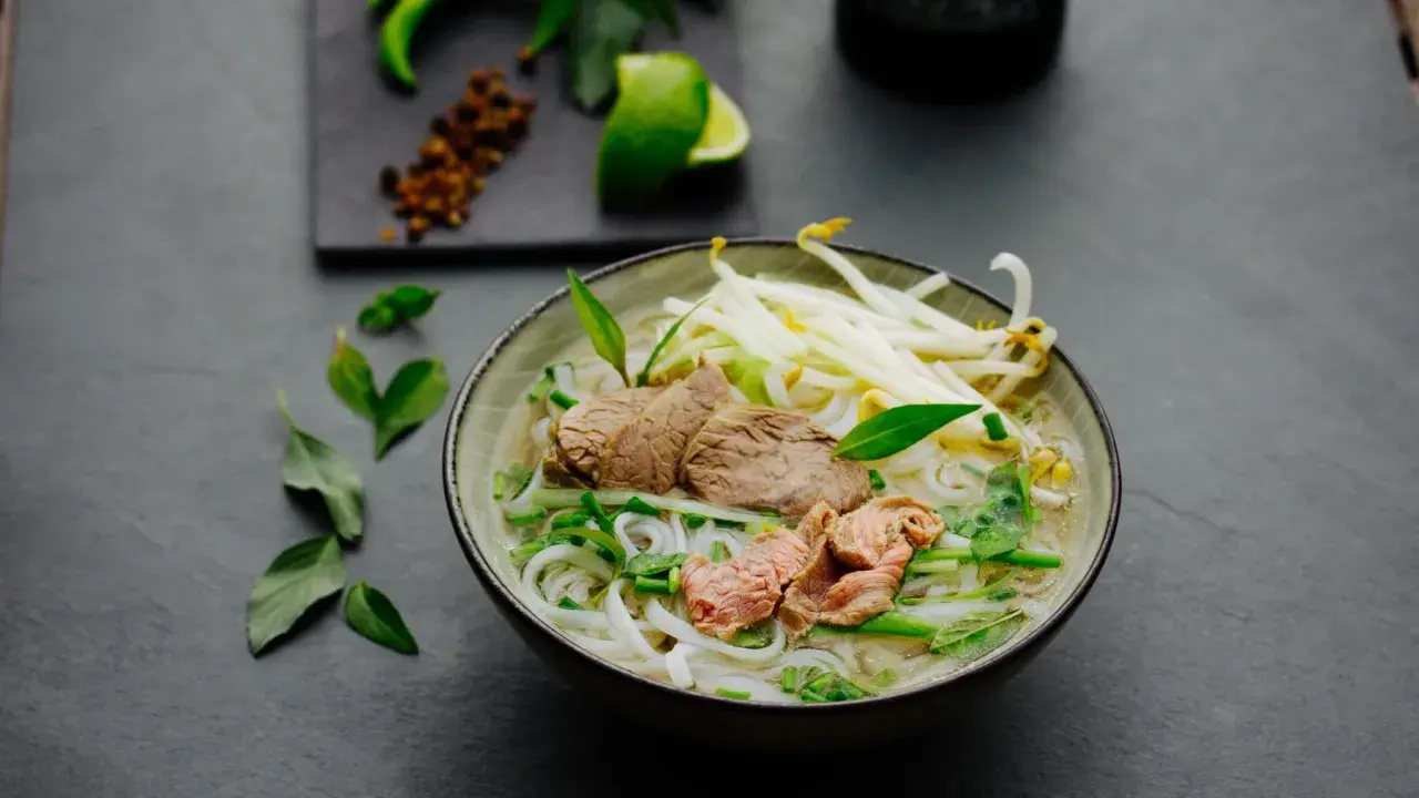 Eine dampfende Schüssel Pho Suppe mit zarten Rindfleischscheiben, Reisnudeln, Sojasprossen und frischen Kräutern.