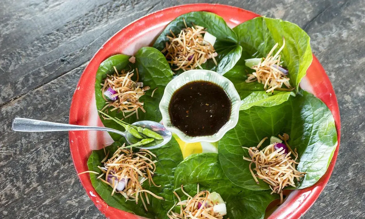 Miang Kham: grüne Blätter gefüllt mit knusprigen Nüssen, Zwiebeln und Limette, serviert mit Dip und Chilis.