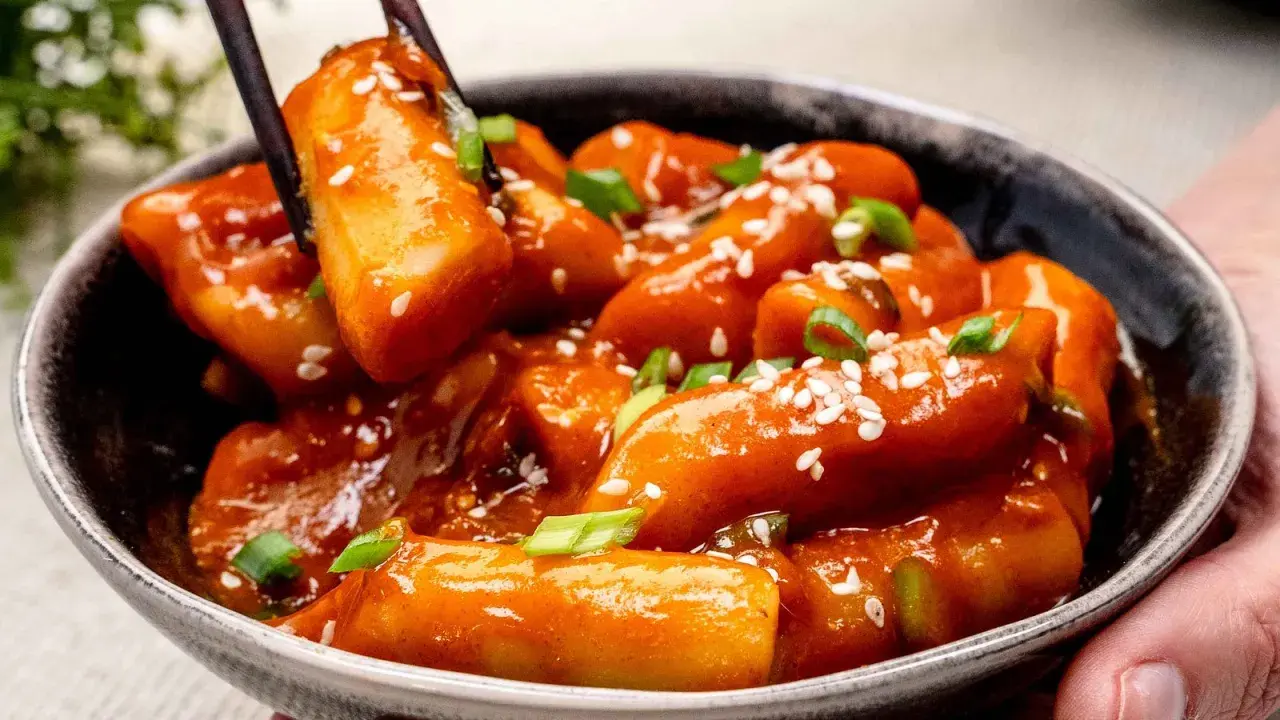 Schüssel mit würzigem Tteokbokki, Reiskuchen in scharfer Sauce, garniert mit Sesam und Frühlingszwiebeln.