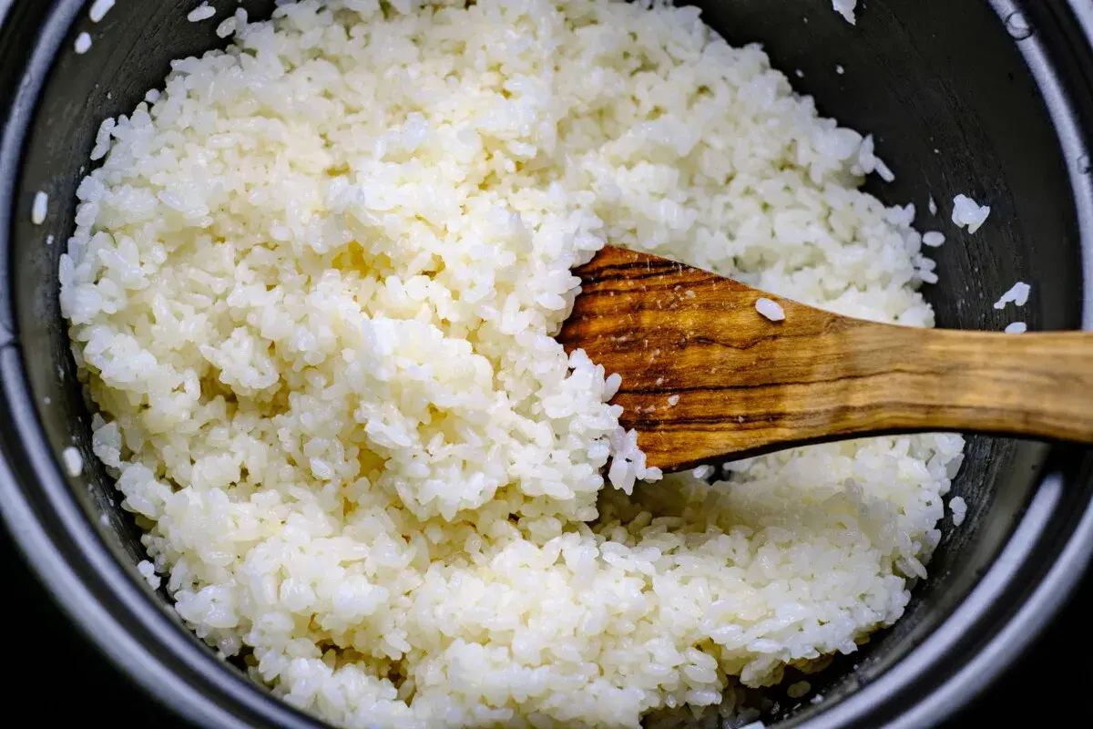 Frisch gekochter Reis wird mit einem Holzlöffel vermischt, bereit für Sushi-Essig.