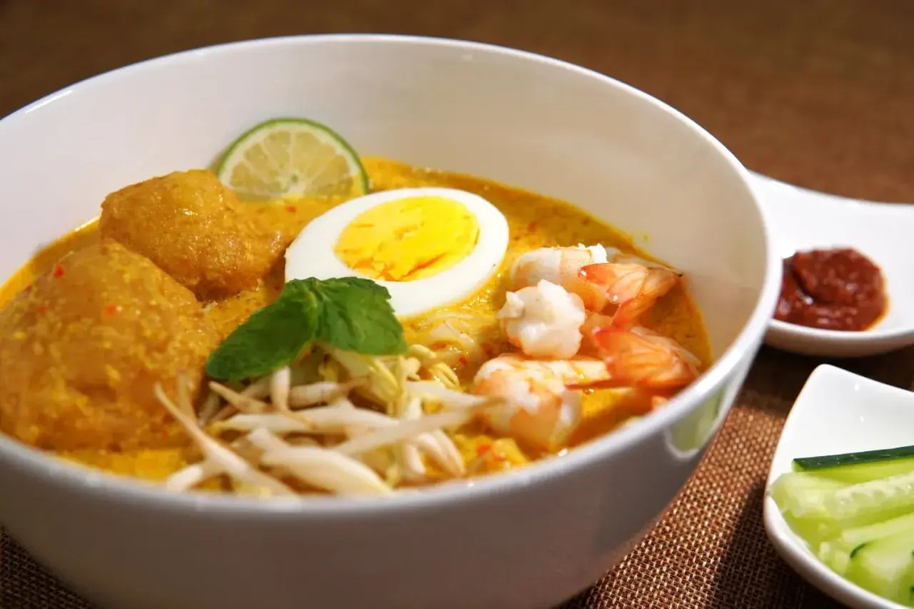 Schüssel mit cremigem Laksa-Rezept, Garnelen, Ei, frischen Sprossen und Limette.