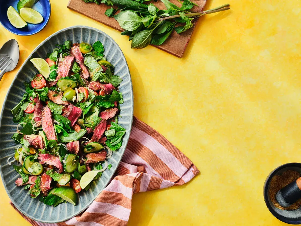 Würzig-frischer Rindfleischsalat Thai mit zarten Rindfleischstreifen, Gurken, Tomaten und Kräutern, garniert mit Limettenspalten.