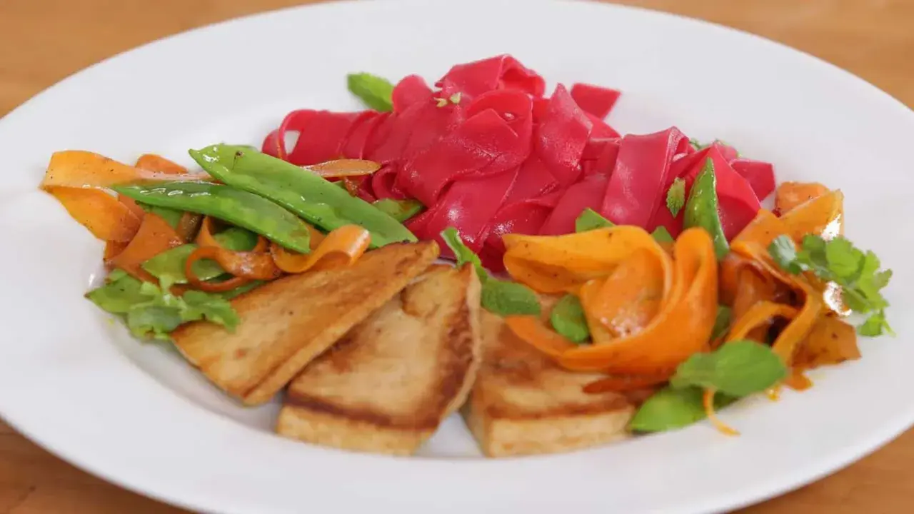Bunte Reisnudeln kochen mit gebratenem Tofu, Karotten und Zuckerschoten. Ein farbenfrohes Gericht, das Lust auf mehr macht.