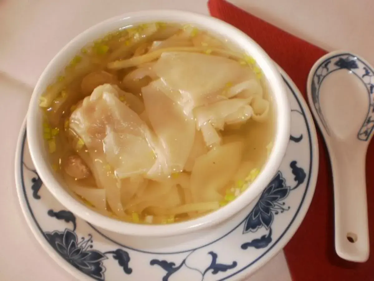 Eine Schüssel mit dampfender Wan-Tan-Suppe, gefüllt mit zarten Teigtaschen und Garnelen, bereit zum Genießen.