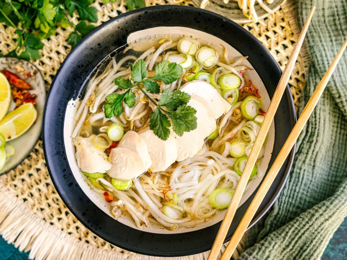 Eine dampfende Schüssel vietnamesische Reissuppe mit zarten Hühnerbrustscheiben, Reisnudeln, Sojasprossen und Frühlingszwiebeln.