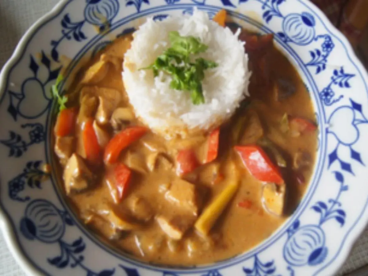 Ein Curry mit Hühnchen, Pilzen und Paprika, serviert mit duftendem asiatischem Reis auf einem blumengemusterten Teller.