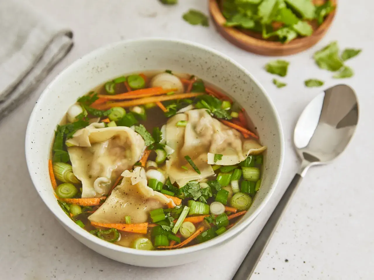 Eine Schüssel mit dampfender Suan La Tang, gefüllt mit Teigtaschen, Karottenstreifen und Frühlingszwiebeln.