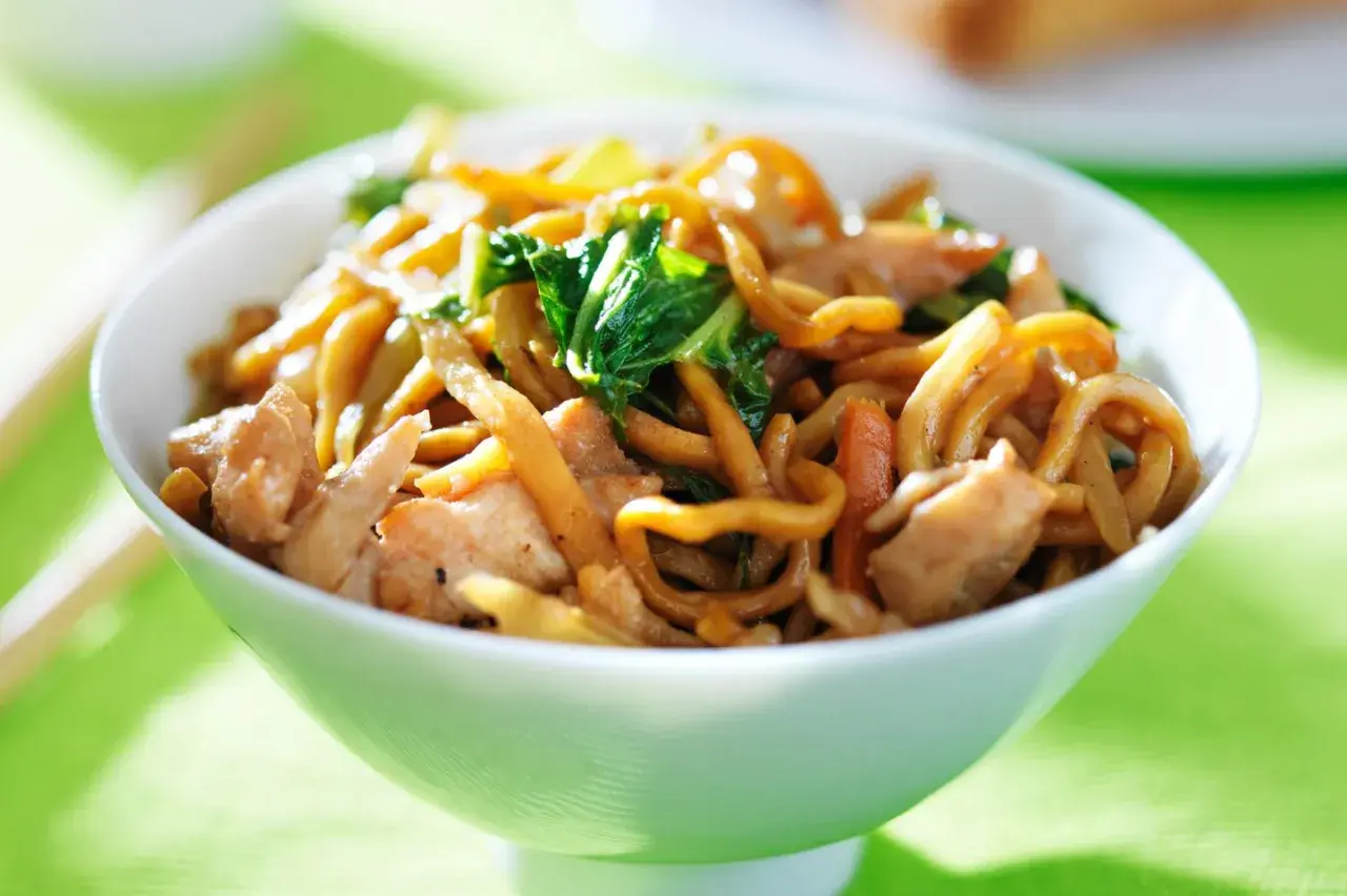 Eine Schüssel mit dampfenden Lo Mein Nudeln, Hühnchen und Gemüse, bereit zum Genießen.
