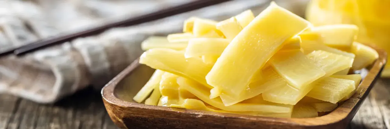 Holzschale mit leuchtend gelben, geschnittenen Bambussprossen, die gesund und appetitlich aussehen. Ein dunkler Löffel liegt im Hintergrund.