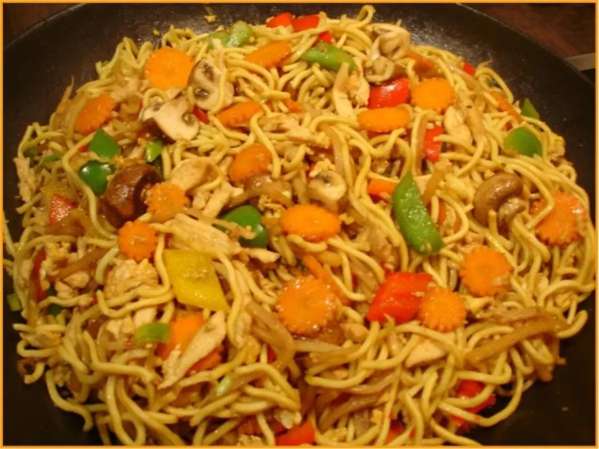 Ein Teller mit leckeren Mi Nudeln, garniert mit Hühnchen, Karotten, Pilzen und Paprika.