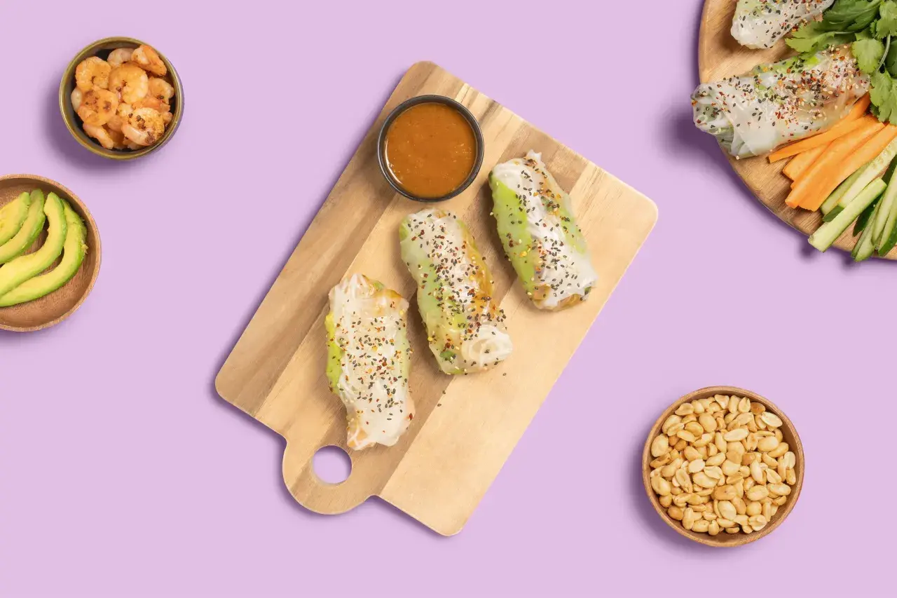 Frische Sommerrollen mit Hoisin-Sauce, Garnelen, Avocado und Erdnüssen auf lila Hintergrund.