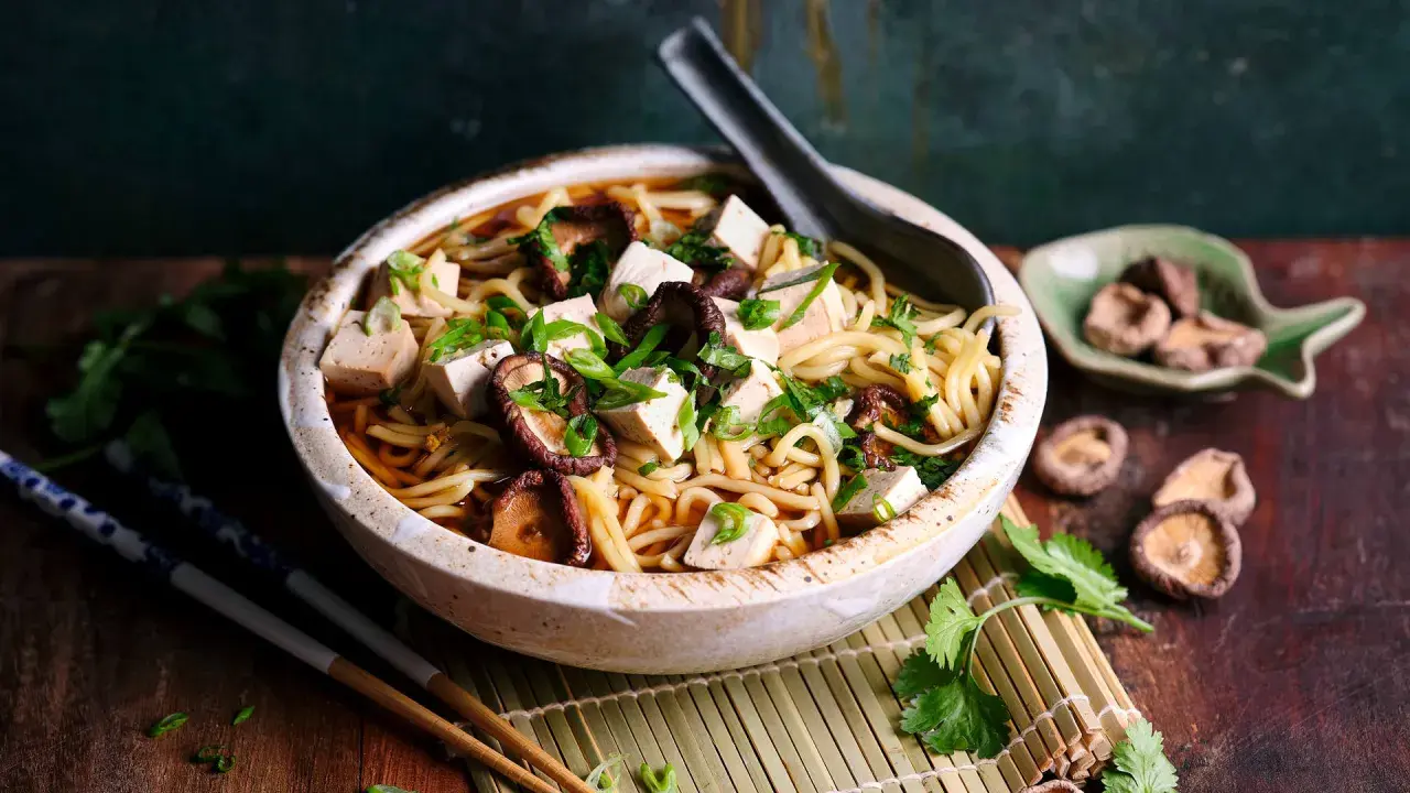 Herzhaftes Shiitake Ramen mit Tofuwürfeln und Frühlingszwiebeln in einer tiefen Schüssel, garniert mit Koriander.