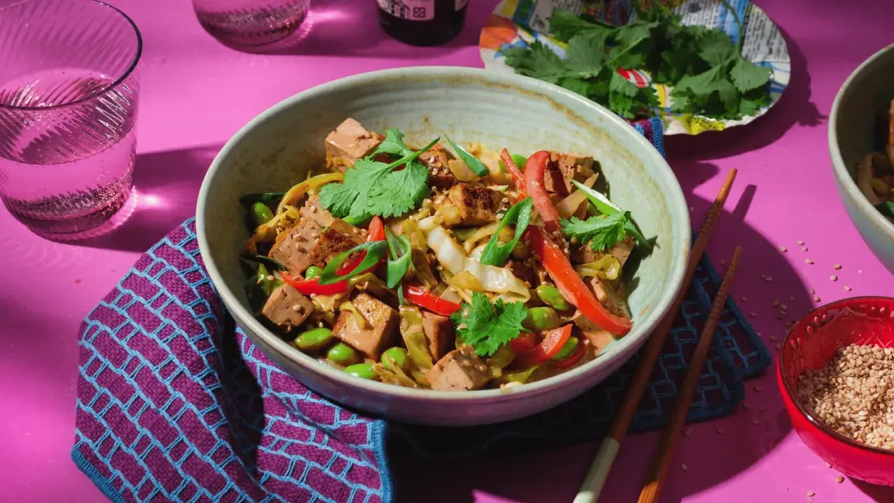 Schüssel mit spitzkohl asiatisch vegetarisch, Tofu, Edamame und Koriander. Dazu Stäbchen und ein Glas Wasser.