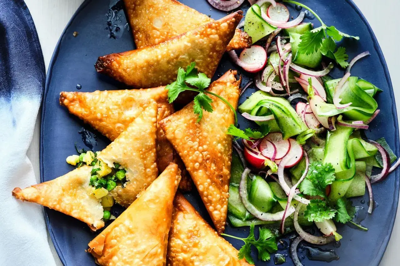 Goldbraune, knusprige Samosas mit Erbsen- und Kartoffelfüllung, serviert mit einem frischen Gurken-Radieschen-Salat. Ein leckeres samosas rezept.