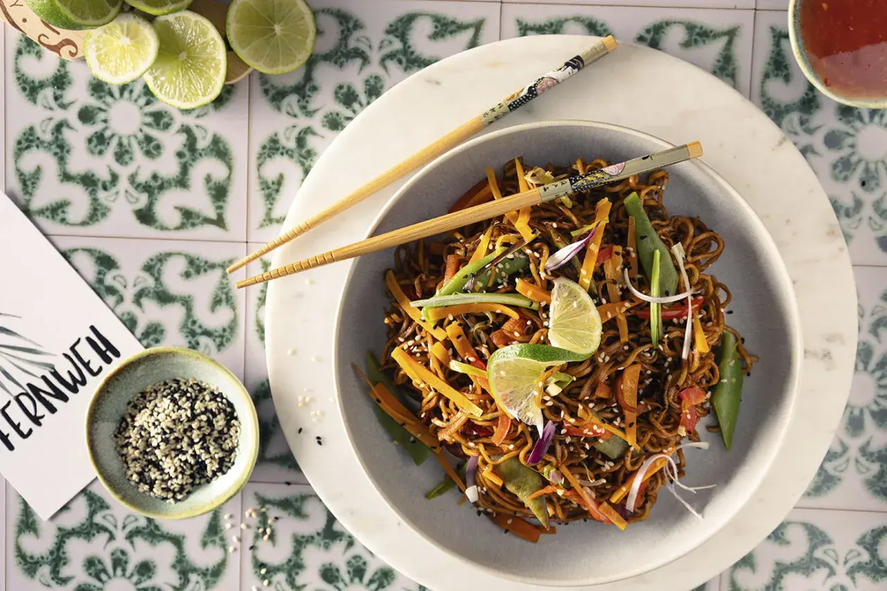 Asia Nudel mit Gemüse und Sesam, garniert mit Limettenspalten. Ein Gericht, das Fernweh weckt.