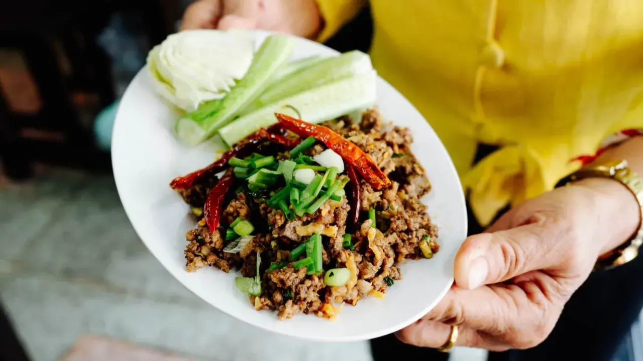 Würziges Laab Moo, ein thailändischer Hackfleischsalat, garniert mit Chili und Frühlingszwiebeln, serviert mit Gurken und Kohl.