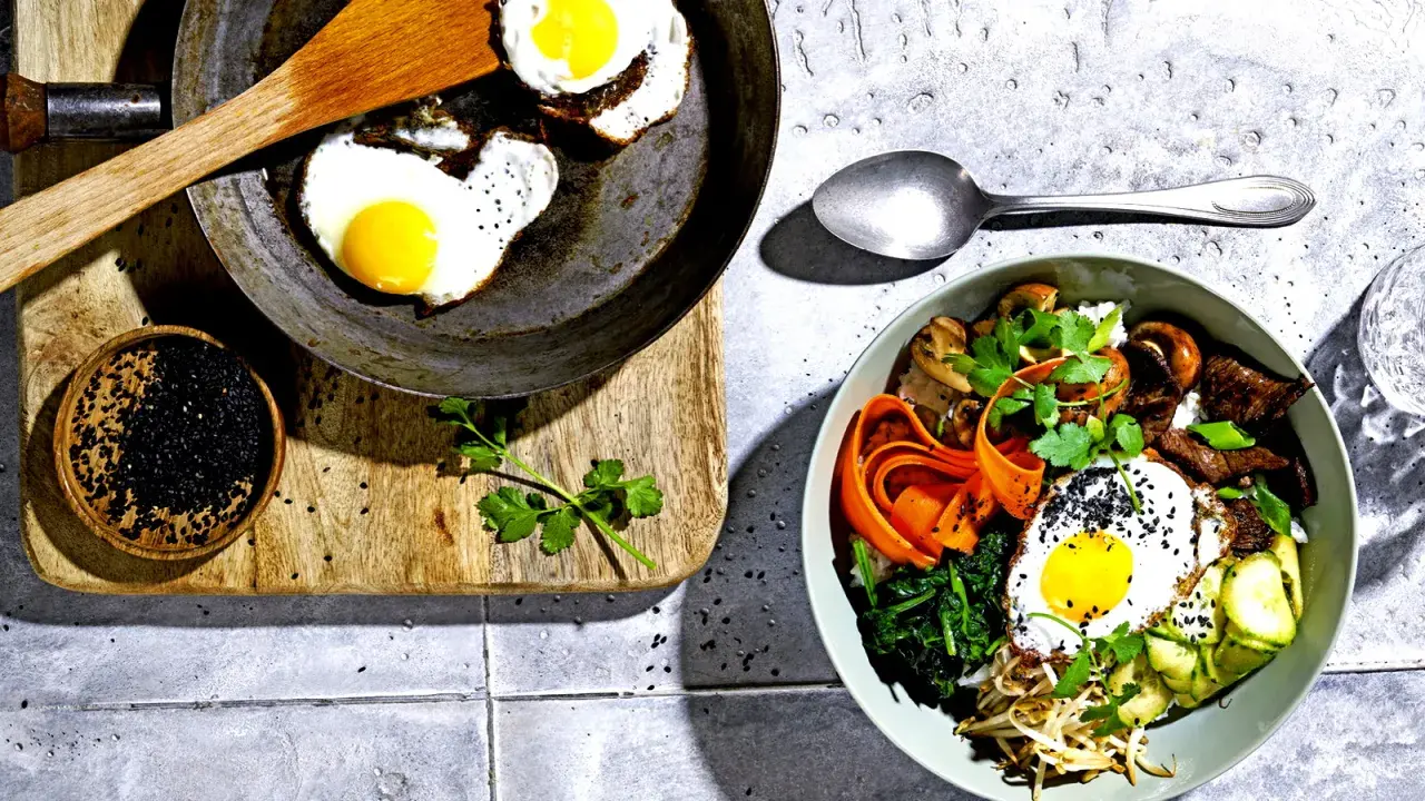 Ein köstliches Bibimbap-Rezept: Bunte Schüssel mit Reis, Gemüse, Rindfleisch, Pilzen und Spiegelei, garniert mit schwarzen Sesamkörnern.