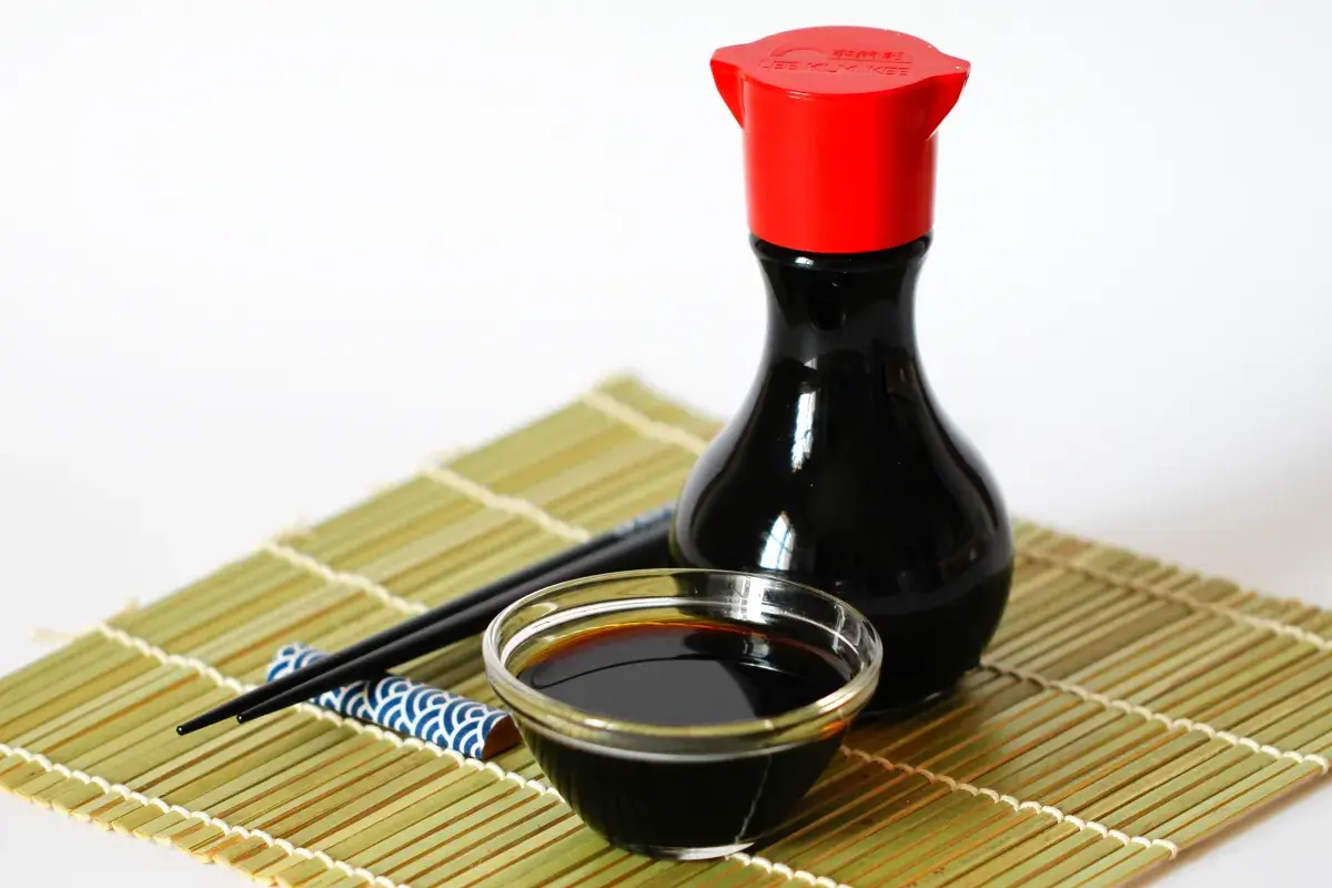 Eine Flasche chinesische Sauce mit Sojasauce, ein Schälchen und Stäbchen auf einer Bambusmatte.