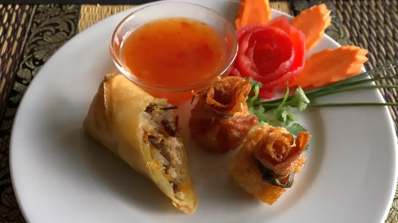 Knusprige Frühlingsrollen und Teigtaschen mit süß-saurer Sauce, garniert mit Karottenblumen. Ein köstlicher Nam Prik Genuss.