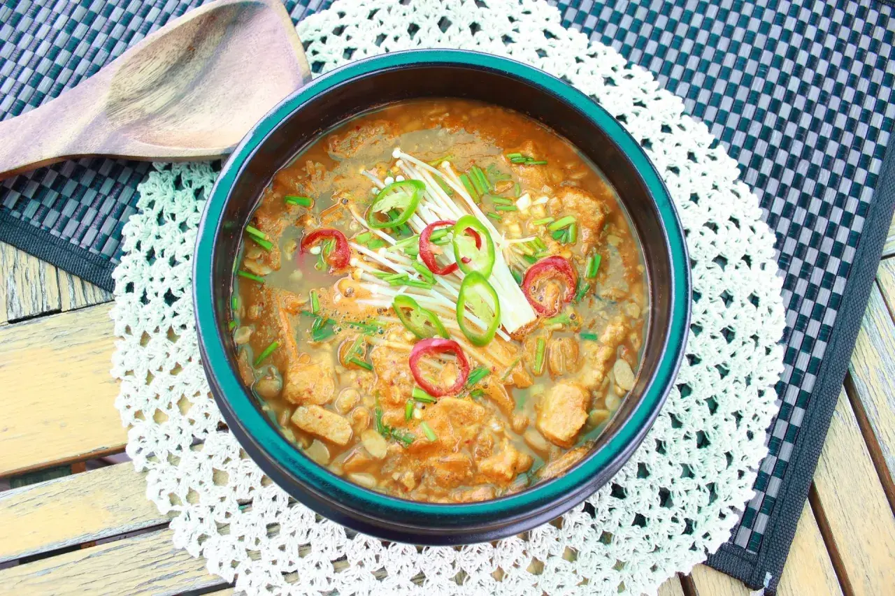 Herzhafter Eintopf mit Doenjang Sauce, Enoki-Pilzen und Chili-Scheiben, serviert in einer Schüssel.