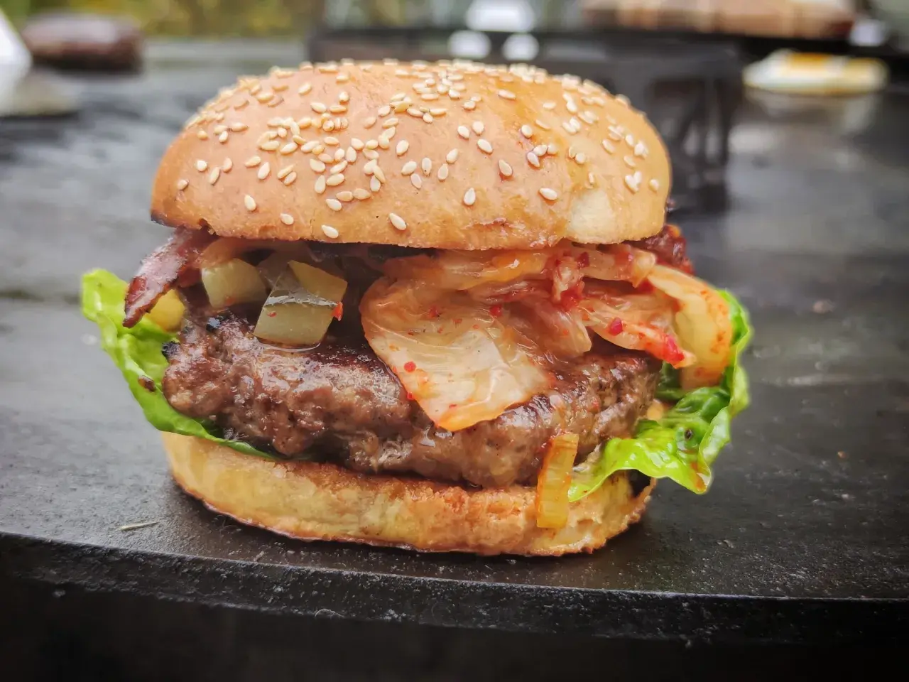 Ein saftiger korean burger mit Kimchi, Gurken und Speck auf einem Sesambrötchen.