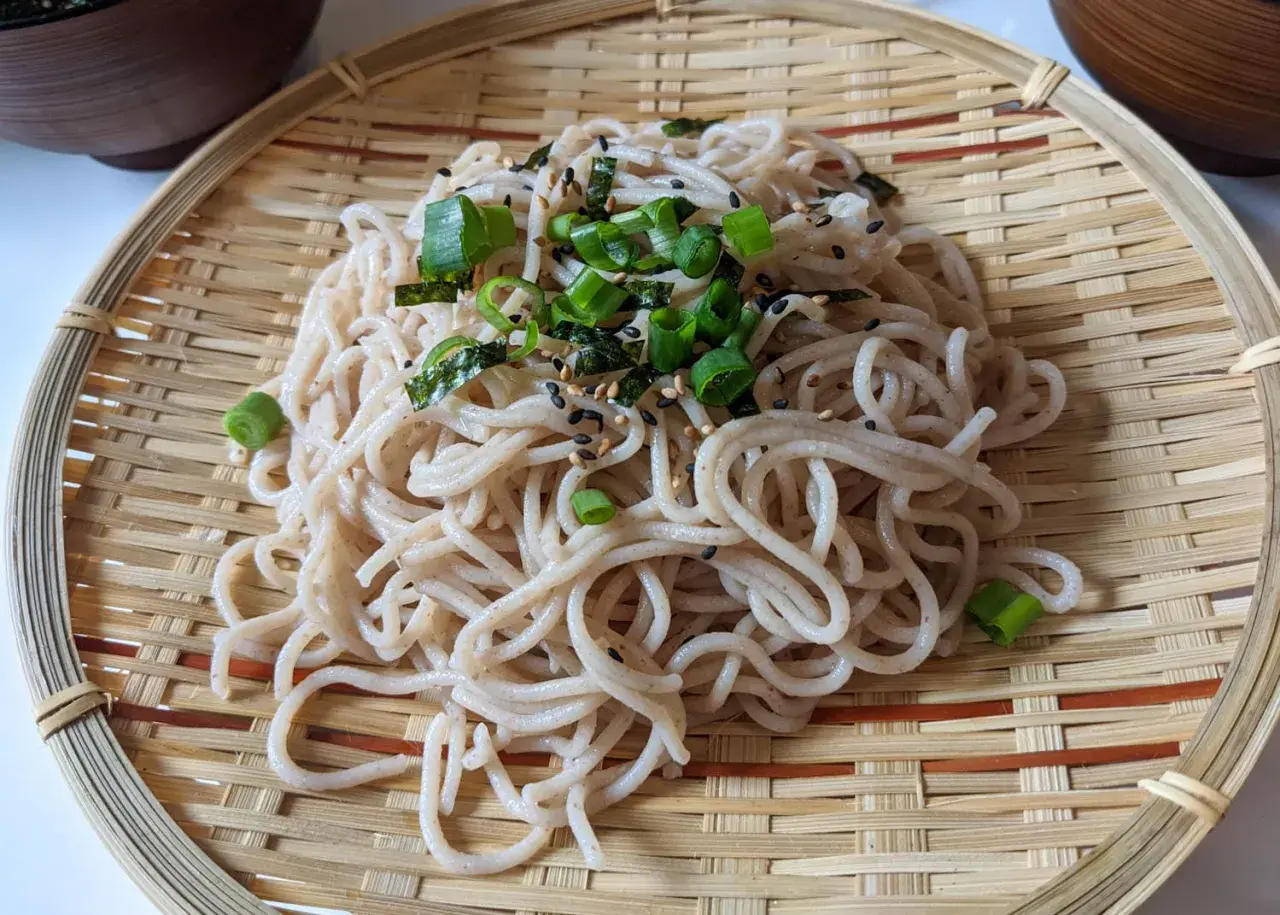 Ein köstlicher soba nudelsalat, garniert mit Frühlingszwiebeln und Sesam, serviert auf einem Bambusteller.