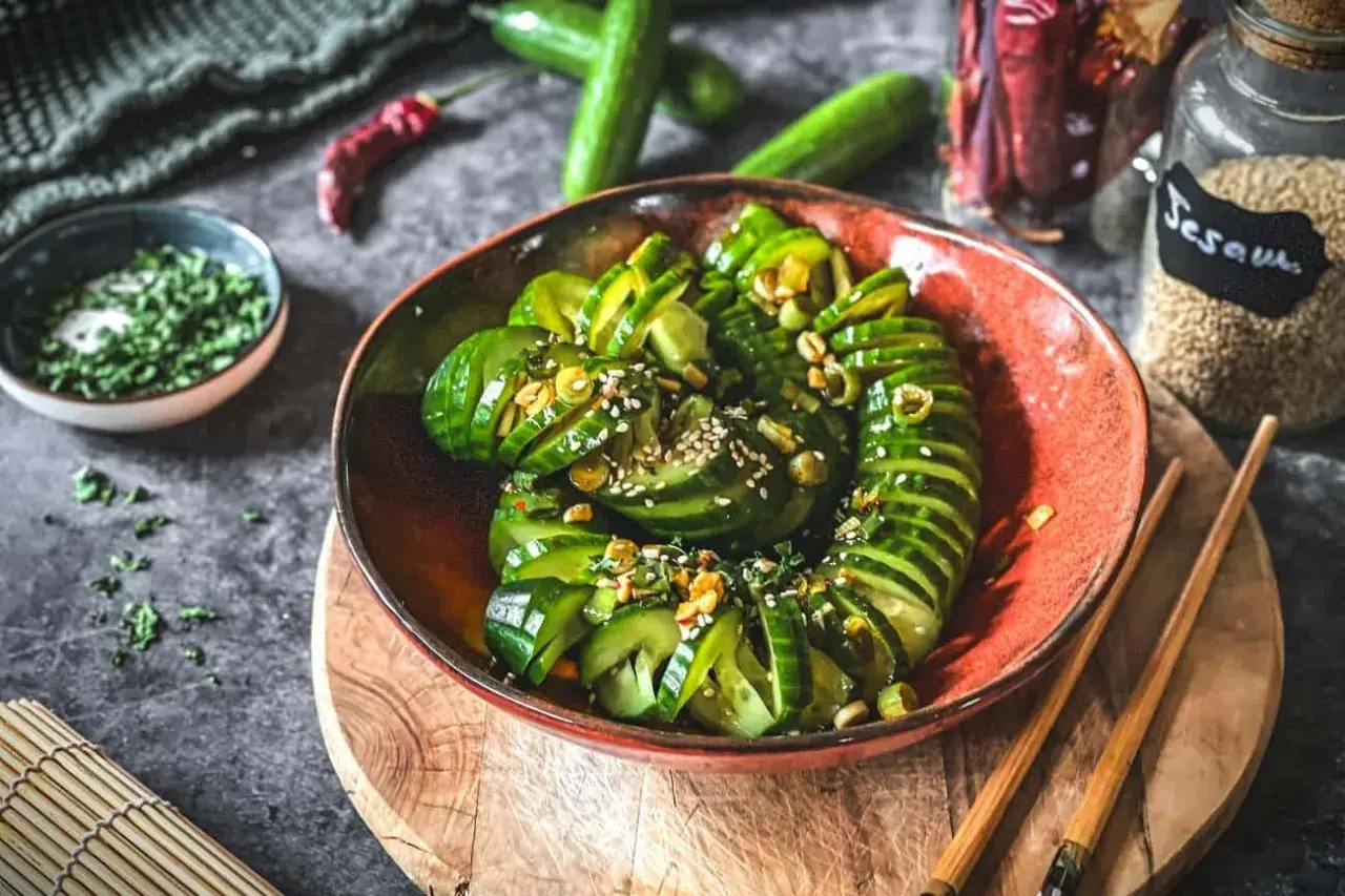 Schmackhafter Gurkensalat asiatisch, garniert mit Sesam und Kräutern, serviert in einer roten Schale mit Stäbchen.