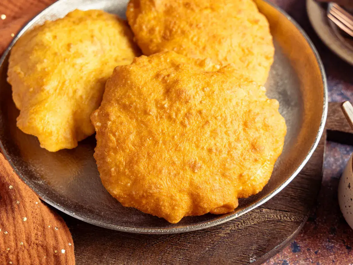 Drei goldbraune, fluffige Bhatura Brote liegen auf einem Teller. Sie sind frisch frittiert und duften herrlich.