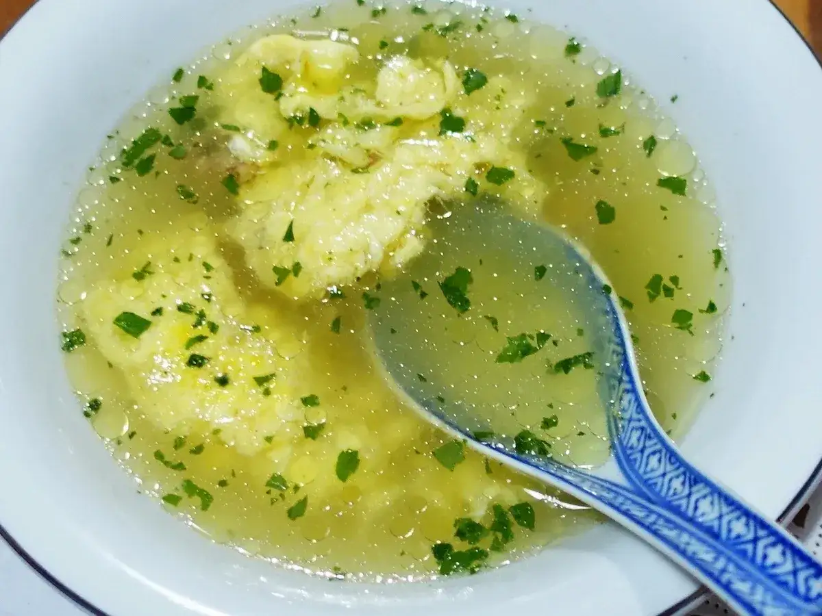 Eine dampfende Schüssel chinesische Suppe mit Ei und frischer Petersilie. Eine blaue Löffel liegt darin.