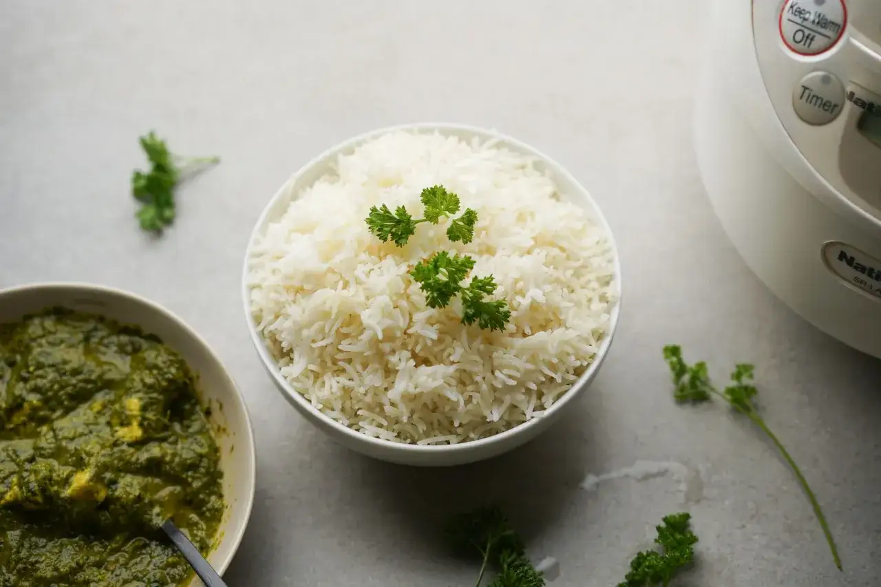 Perfekt gekochter Basmati Reis im Reiskocher, garniert mit Petersilie, neben einer Schüssel grünen Currys.