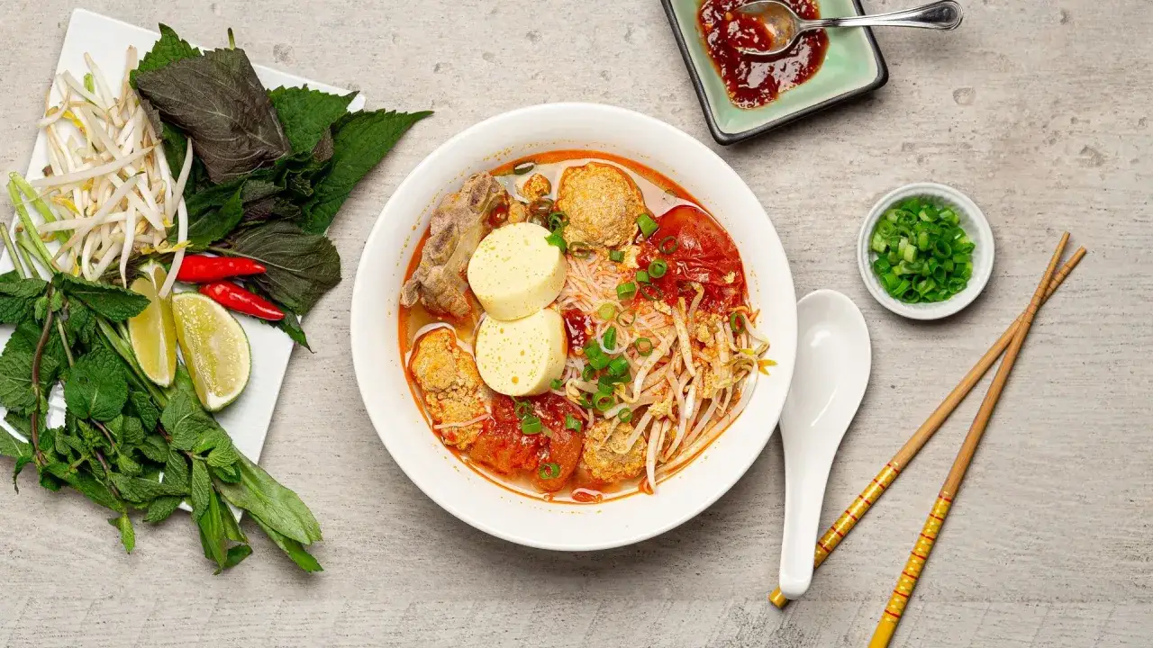 Herzhaftes Bun Rieu mit Fleischbällchen, Tofu, Tomaten und Kräutern. Dazu Reisnudeln in würziger Brühe.