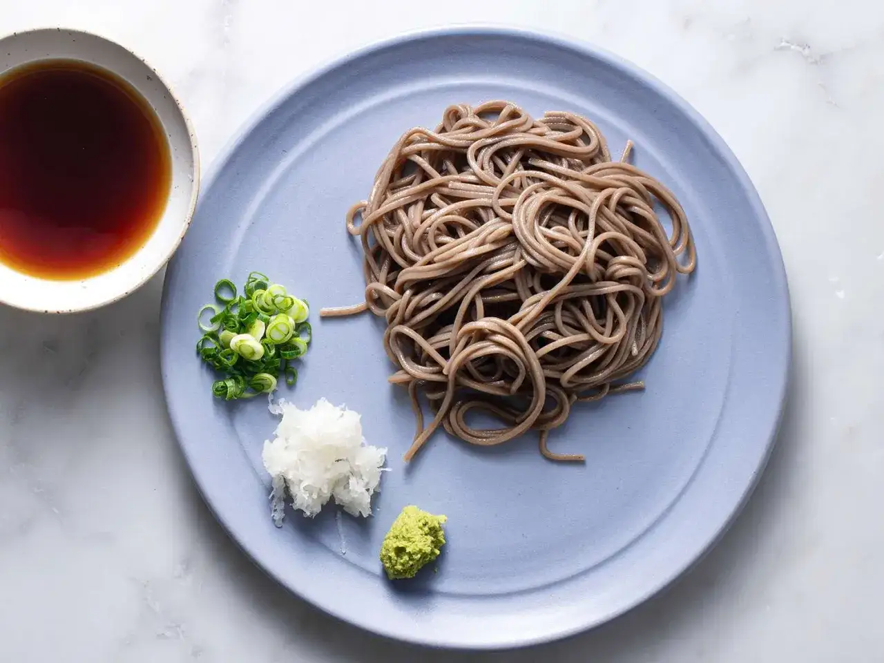 Kalte Soba-Nudeln auf einem Teller mit Sojasauce, Fr&uuml;hlingszwiebeln, geriebenem Rettich und Wasabi.