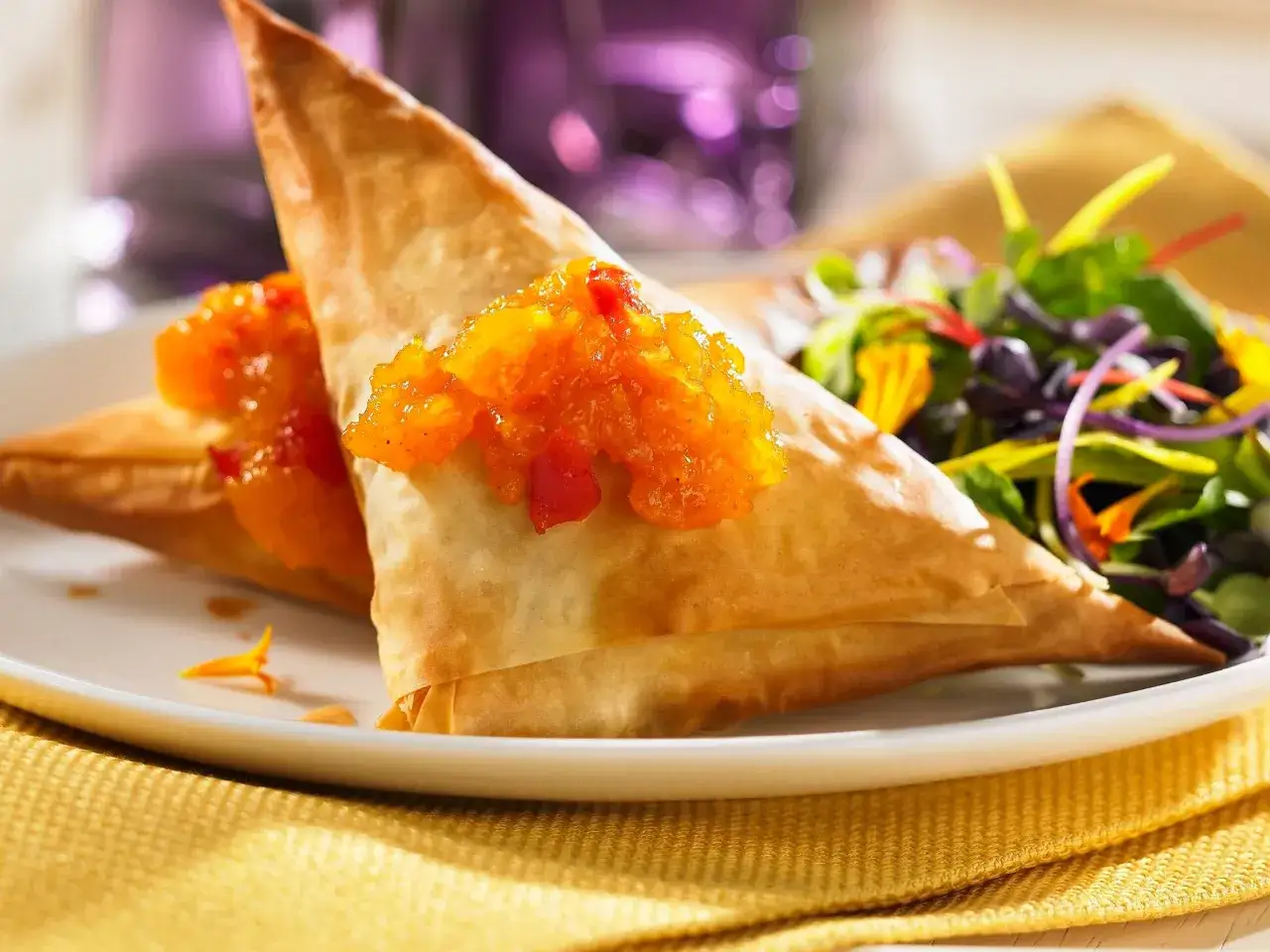 Zwei goldbraune Samosas mit fruchtigem Topping, serviert mit einem bunten Salat. Ein köstliches samosas rezept zum Nachmachen.