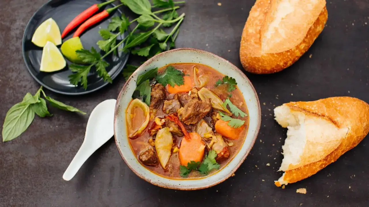 Herzhaftes Bo Kho, ein vietnamesischer Rindfleischeintopf mit Karotten und Zwiebeln, serviert mit knusprigem Baguette und frischen Kräutern.